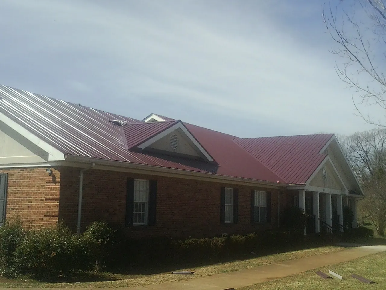 Red metal roof with gabled entries on a long brick building, from a Hail Damage Roof Repair job in Chesapeake