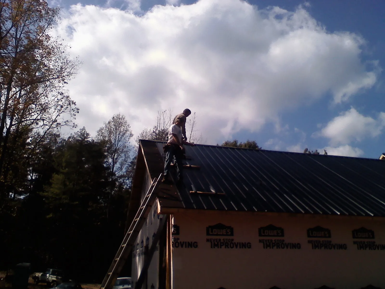 Roofer fastening dark metal panels high against a cloudy sky, from a Roof Inspection job in Chesapeake